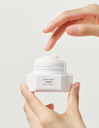 Hand holding a white cream jar with visible brand name on a light gray background