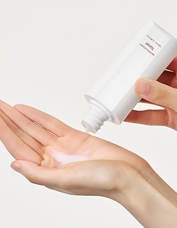 Hand applying a white cream from a tube labeled 'JUNO' on a light background